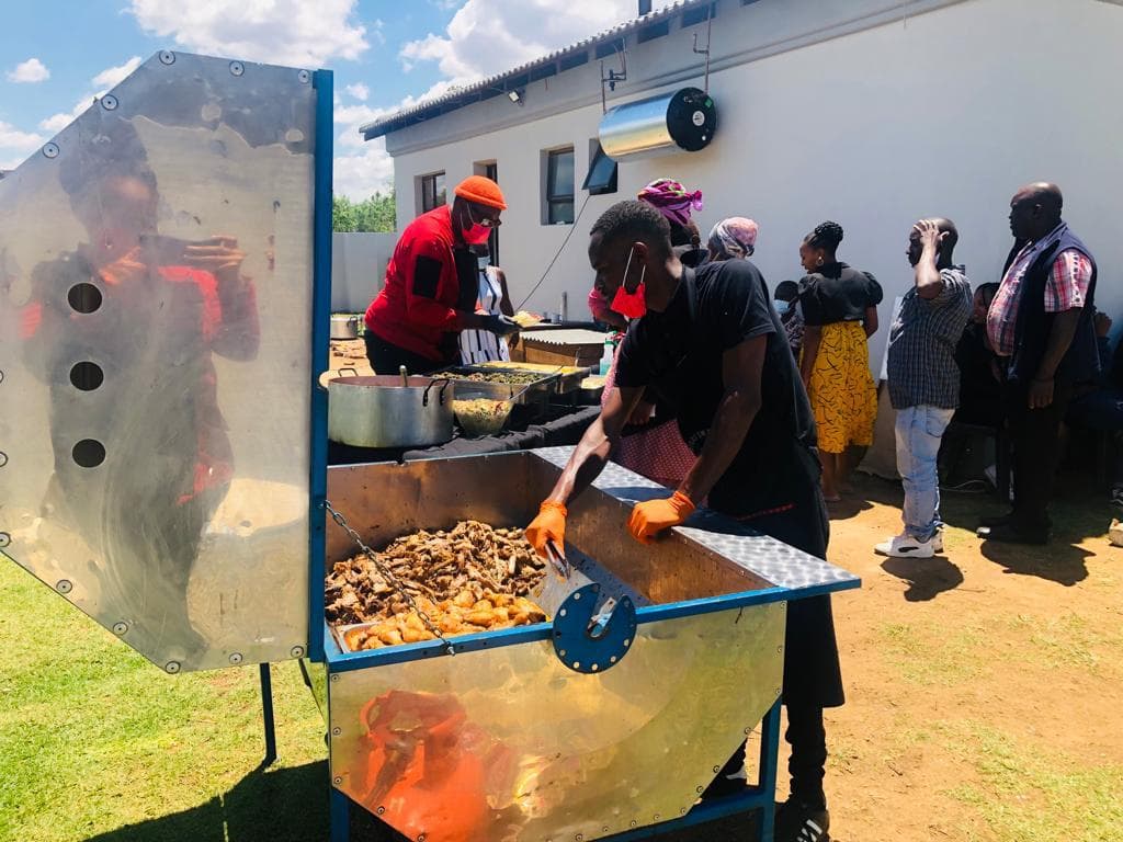 The team serving hot food from the spit trailer as people queue alongside.