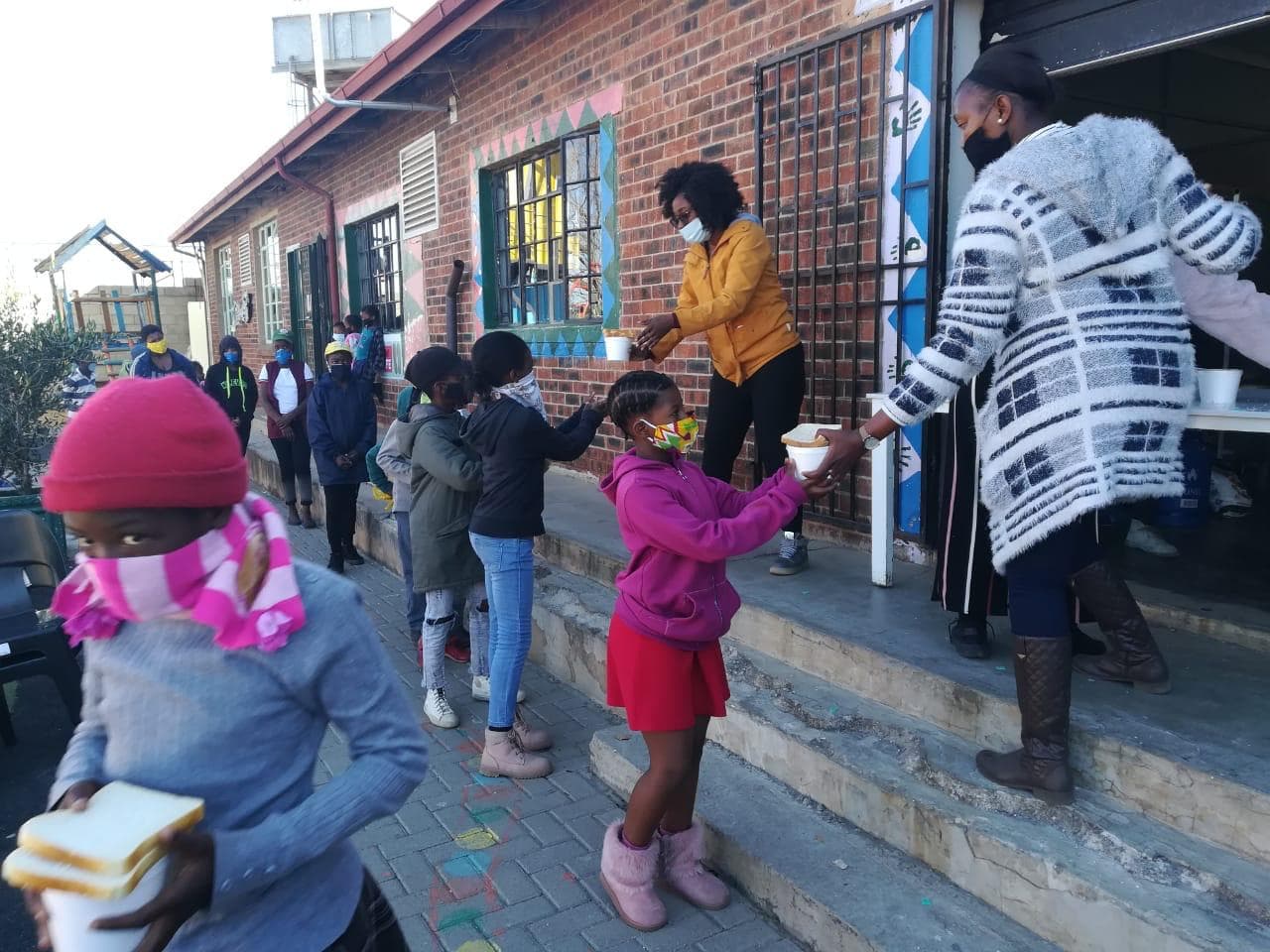 Children queuing outside as servers hand out cups of hot food and bread.