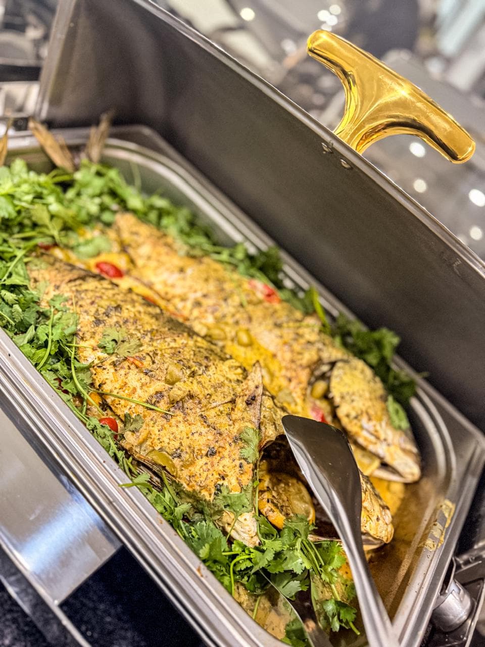 A whole roasted fish, herb and chilli crusted, in a chafing dish.