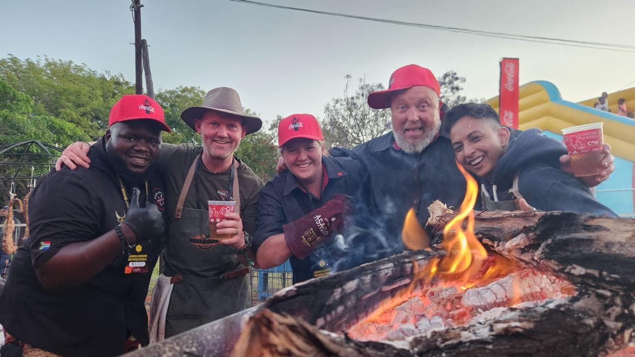 Biggy and four other chefs and friends gathered around an open fire, drinks in hand.