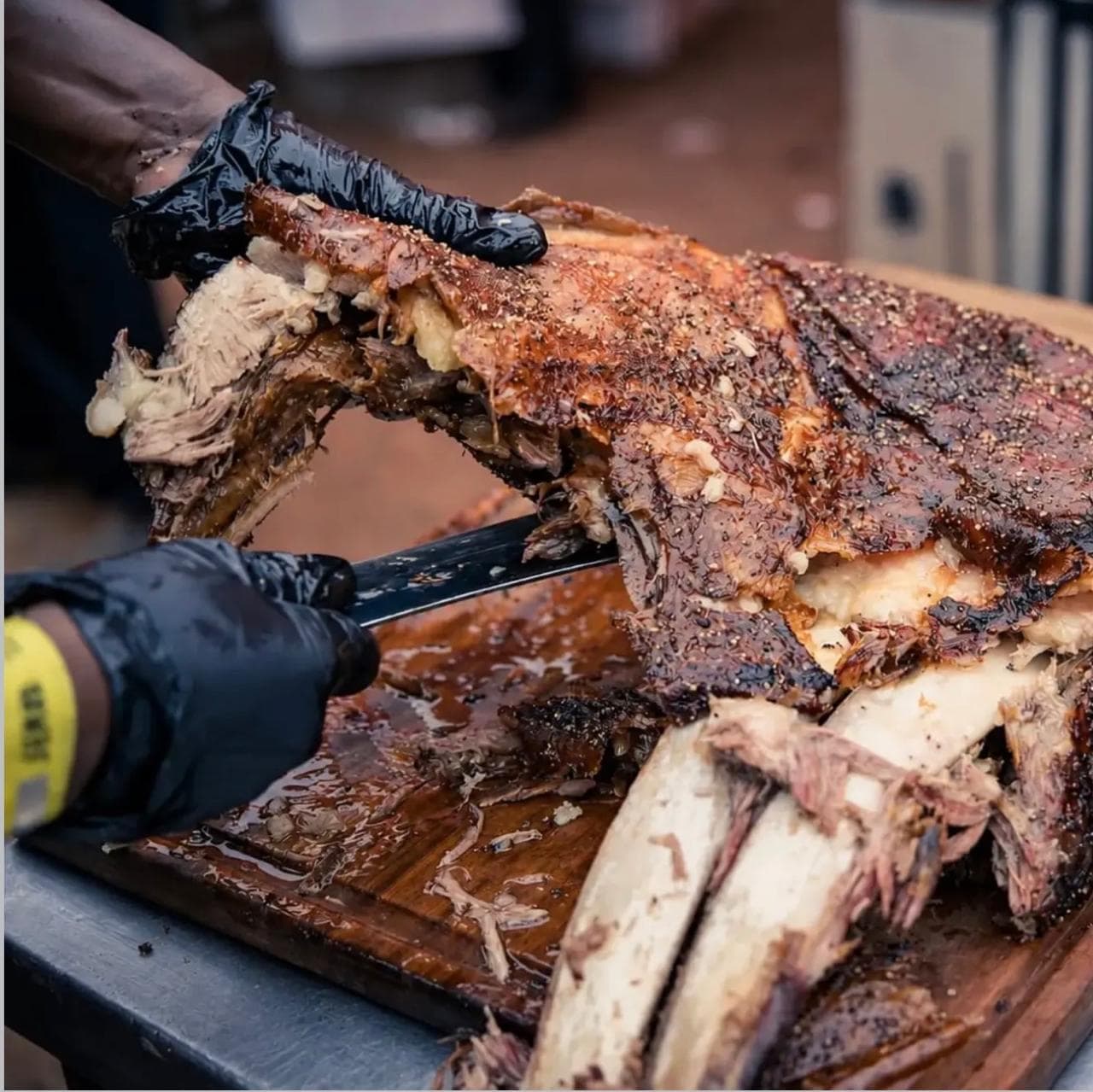 Close-up of hands carving a rack of glazed, seasoned ribs on a wooden board.