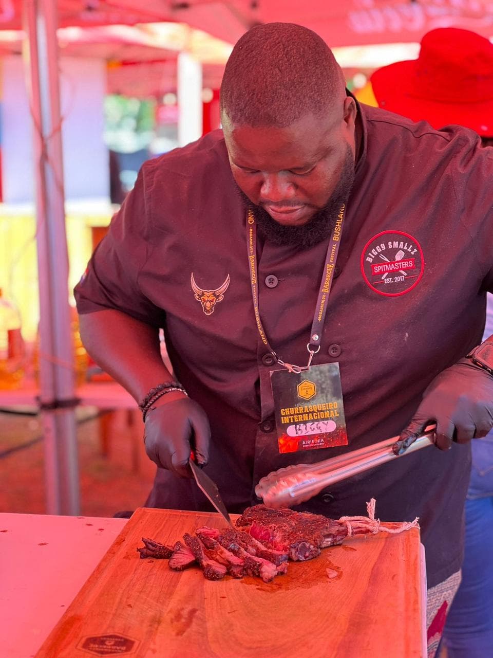 Biggy slicing grilled meat on a wooden board, red festival lighting.