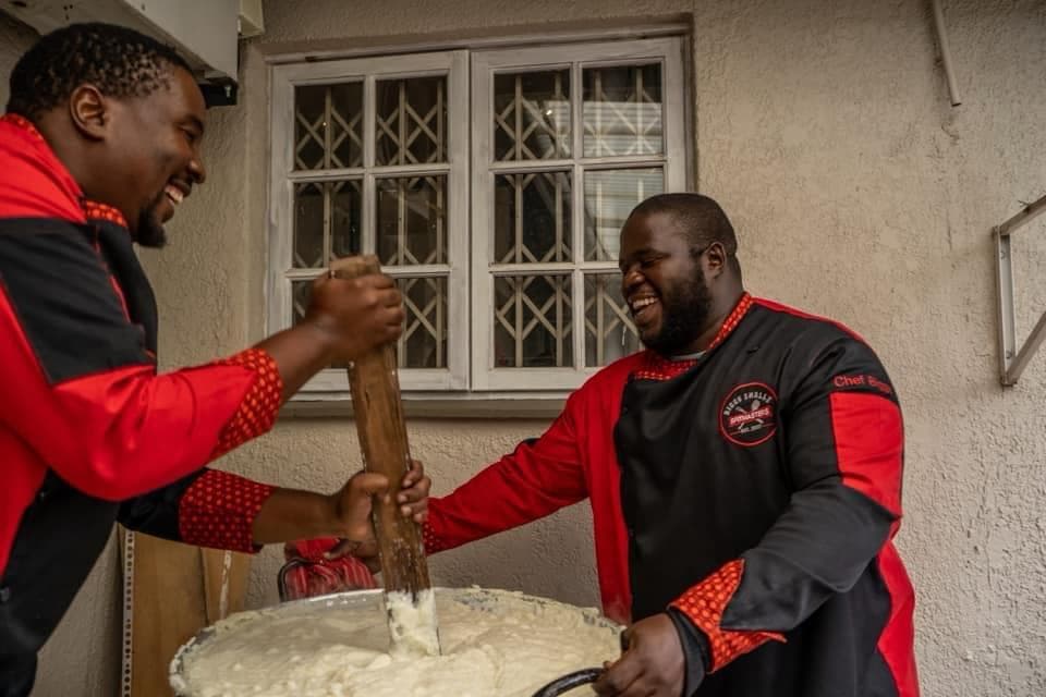 Two of the crew laughing while pounding pap together, in the earlier uniform.
