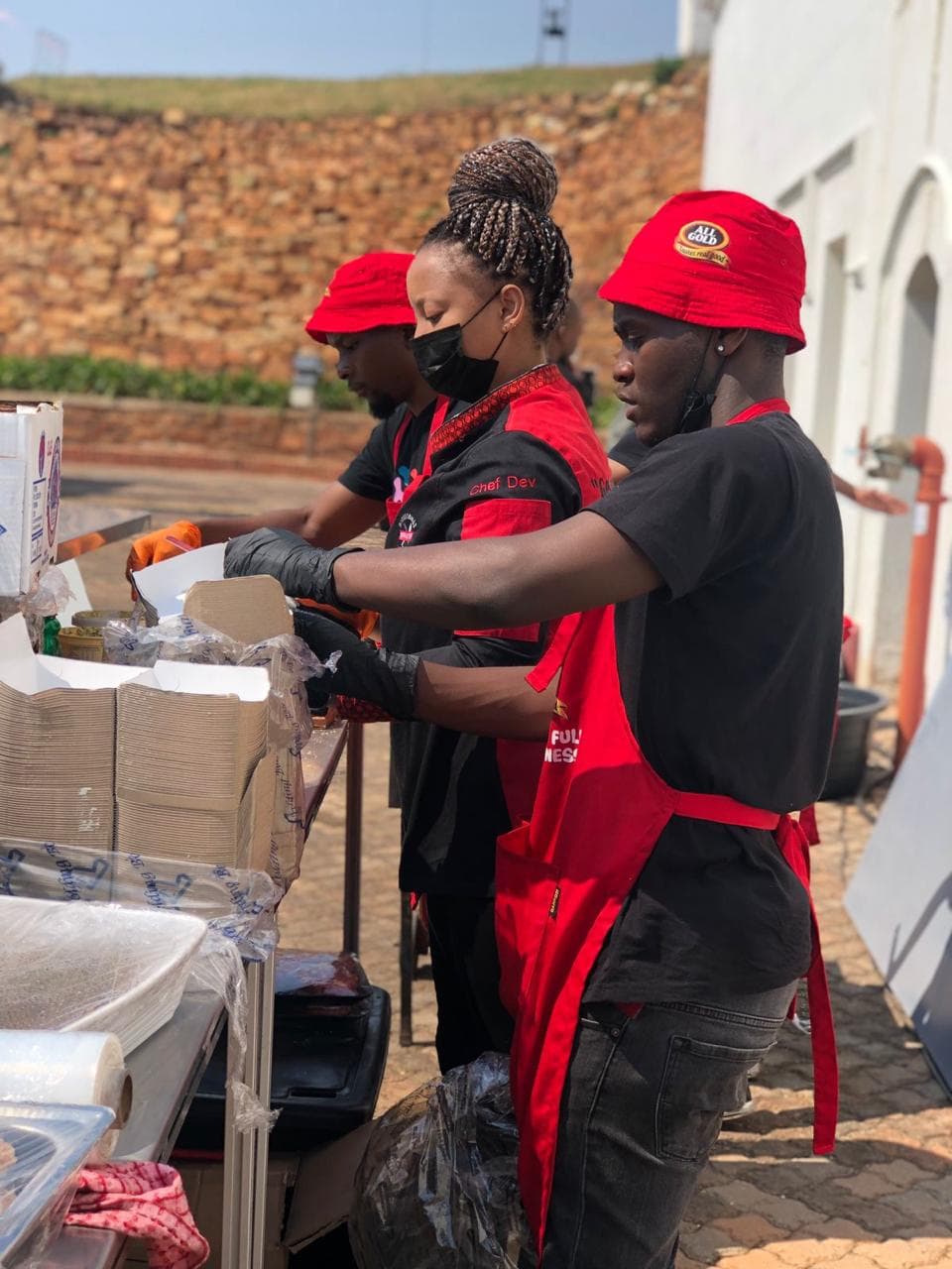 The crew prepping orders at an outdoor stall, in All Gold-branded aprons for a sponsor event.