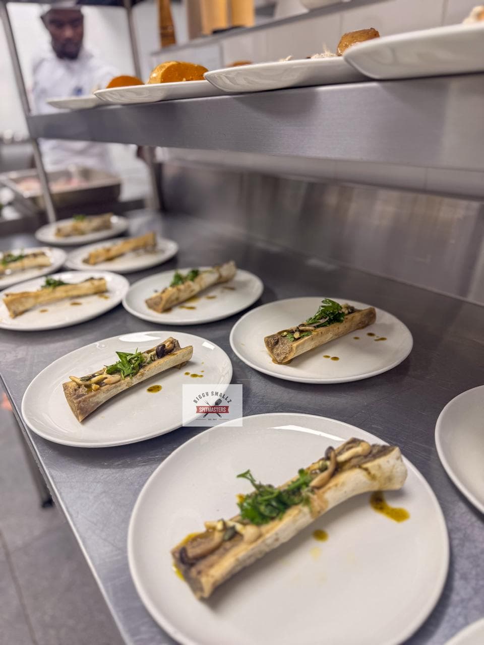 Roasted marrow bones with herbs and oil, plated across the pass.